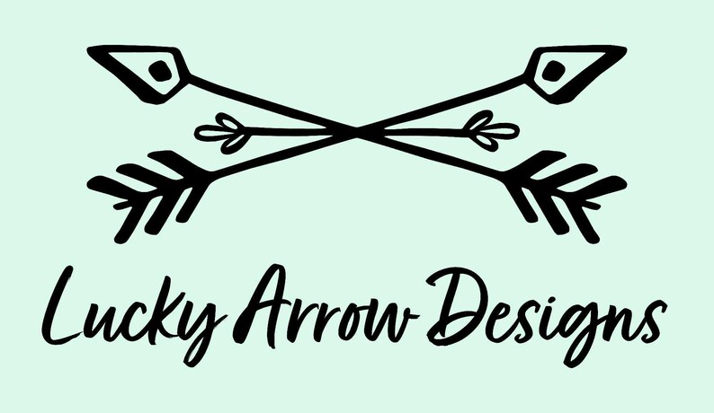 K&ouml;nnte beinhalten: Schwarz gekreuzte Pfeile mit dekorativen Details und dem Text "Lucky Arrow Designs" in Schreibschrift auf hellgr&uuml;nem Hintergrund. Die Pfeile haben eine Stammes- oder Boho-&Auml;sthetik.