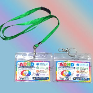 May include: A green lanyard attached to a clear plastic badge holder and a separate clear plastic badge holder with a silver metal keyring. Both holders contain a card with the text ADHD PLEASE BE UNDERSTANDING, DIFFERENT NOT LESS.