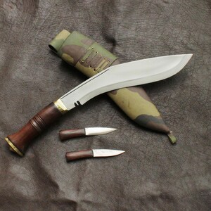 May include: A large, curved blade knife with a wooden handle and a smaller knife, both with sheaths. The blade is silver, and the handle is brown with a brass accent. The sheath is camouflage.