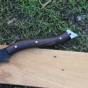 May include: A black axe with a dark brown wooden handle and silver accents. The axe is lying on a wooden surface.