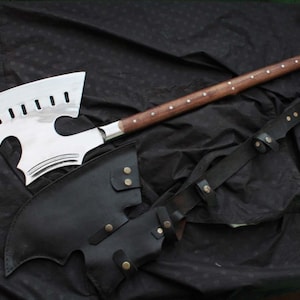 以下が含まれることがあります： 木製の柄と黒い革の鞘が付いた、大きな銀色の斧。 斧頭は、いくつかの切り欠き穴があるユニークな湾曲した形状をしています。 ハンドルは、銀色のスタッドが付いた茶色です。