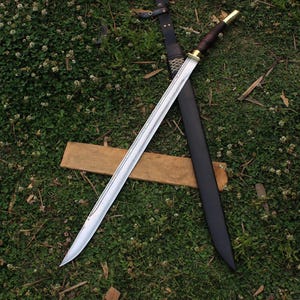 Pu&ograve; includere: Una spada argentata con un manico in legno e un fodero in pelle nera. La spada &egrave; appoggiata su una superficie in legno e uno sfondo di erba verde.
