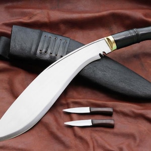 May include: A large, curved blade knife with a black handle and a leather sheath. Two smaller knives with wooden handles are also present. The blade is silver, and the handle has gold accents. The knife is displayed on a brown leather surface.