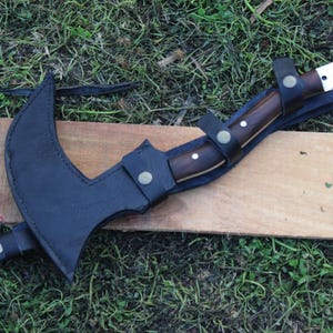 May include: A black leather sheath with a brown wooden handle knife attached. The knife has a silver blade and is secured to the sheath with a strap.