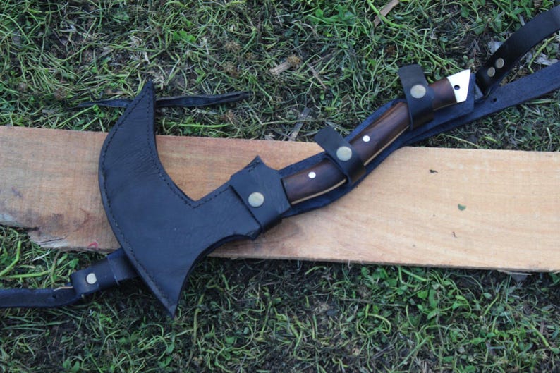 May include: A black leather sheath with a brown wooden handle knife attached. The knife has a silver blade and is secured to the sheath with a strap.