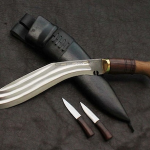 May include: A large, curved blade knife with a wooden handle and a leather sheath. Two smaller knives with wooden handles are also present. The blade has a silver finish with decorative lines. The handle is a dark brown color with a brass accent.