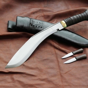May include: A large, curved blade knife with a black handle and a leather sheath. Two smaller knives are also present. The blade is silver, and the handle has a dark, textured grip. The sheath is black.