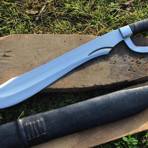 May include: A silver-colored sword with a black leather handle and a black leather sheath. The sword has a curved blade and a large, circular guard.