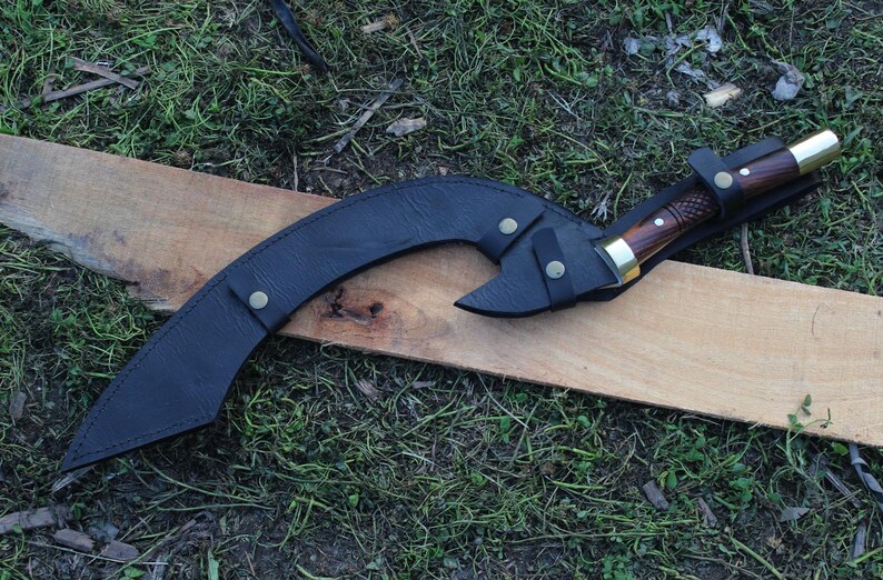 May include: A black leather scabbard with a curved blade and a wooden handle. The scabbard has a brass button closure and a decorative design.