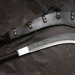 May include: A curved blade knife with a decorative etched pattern on the top edge, and a black wrapped handle. The knife is paired with a black leather sheath with brass-colored rivets and a strap.