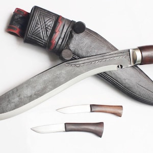 May include: A large, curved blade knife with a wooden handle and a leather sheath. Two smaller knives with wooden handles are also present. The sheath is black with red accents and decorative stitching. The knife blades have a silver finish.