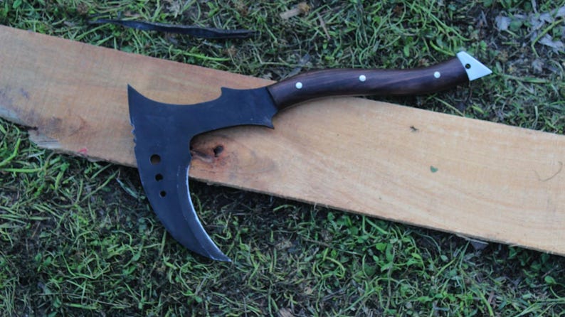 May include: A black curved axe with a wooden handle and white accents. The axe is lying on a wooden surface.