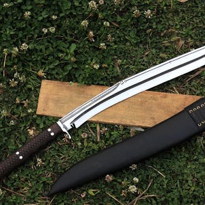 May include: A long, curved, silver blade with a brown wooden handle and a black leather sheath. The blade has a decorative pattern etched into it.