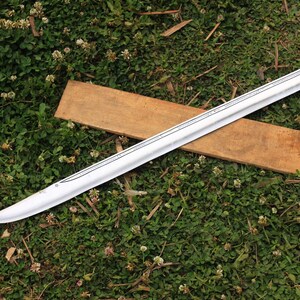 Pu&ograve; includere: Una spada d'argento con una guaina di legno che giace su un letto di erba verde con fiori di trifoglio bianco.