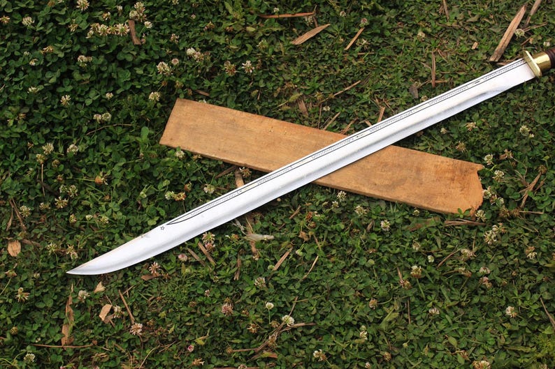 Pu&ograve; includere: Una spada d'argento con una guaina di legno che giace su un letto di erba verde con fiori di trifoglio bianco.