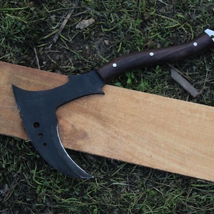 May include: A black axe with a curved blade and a wooden handle. The axe is lying on a wooden surface.