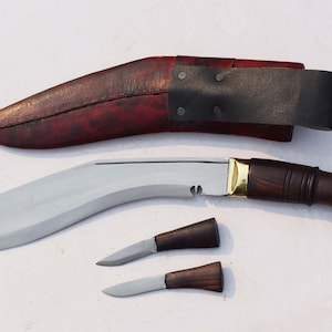 May include: A large, curved blade knife with a wooden handle and two smaller knives. The blade is silver, the handle is dark brown with gold accents, and the sheath is red-brown leather with a black leather strap.