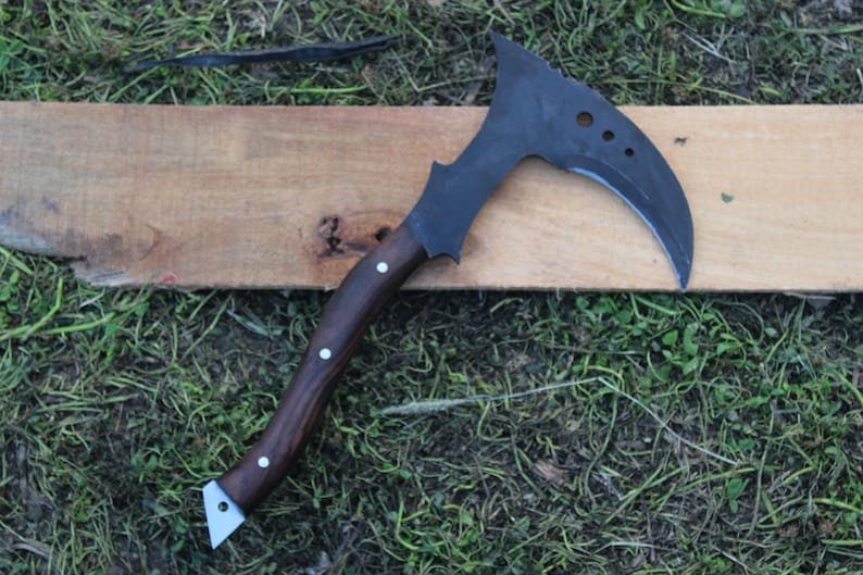 May include: A black and brown curved axe with a wooden handle. The axe is resting on a wooden surface.