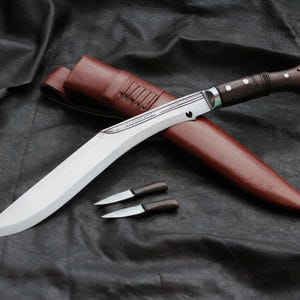May include: A large, curved blade knife with a wooden handle and a brown leather sheath. Two smaller knives with wooden handles are also present. The blades are silver, and the handle is dark brown. The sheath is a reddish-brown color.