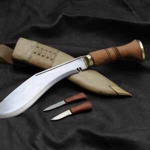 May include: A large, curved blade knife with a wooden handle and brass accents, resting on a leather sheath. Two smaller knives with wooden handles are also present. The blades are silver, and the handles are brown.