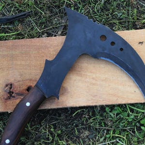 May include: A black curved knife with a wooden handle. The knife has a serrated edge and several holes in the blade.