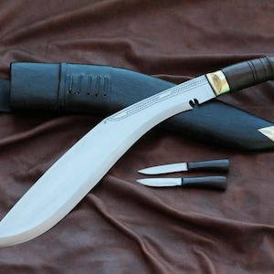 May include: A large, curved blade knife with a wooden handle and brass accents, accompanied by a black leather sheath and two smaller knives. The blade is silver, and the handle is dark brown.