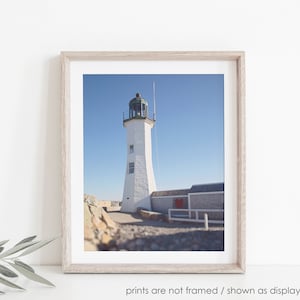 May include: A white lighthouse with a green roof stands tall against a clear blue sky. The lighthouse is surrounded by rocks and a stone wall.