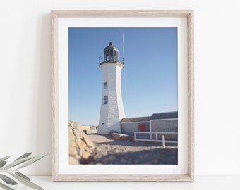 May include: A white lighthouse with a green roof stands tall against a clear blue sky. The lighthouse is surrounded by rocks and a stone wall.