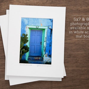 May include: A photograph of a blue door with a horseshoe above it. The door is surrounded by a green cactus and a blue wall. The door has a number "518" on it. The photograph is matted in white acid-free mat board and is available in 5x7 and 8x10 sizes.