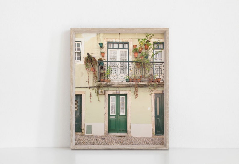 May include: A photograph of a building with a balcony and green doors. The balcony is decorated with potted plants and flowers. The building is painted in a light green color.