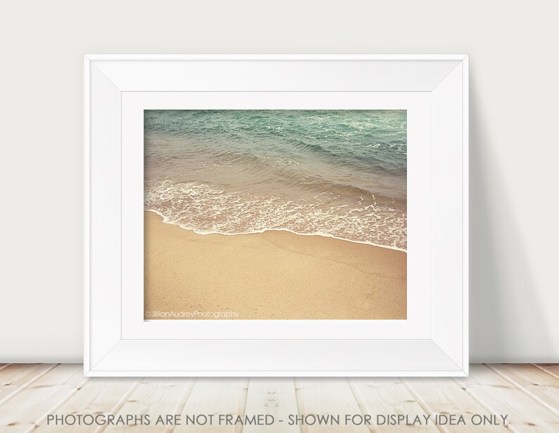 May include: A photograph of a beach scene with blue water and white waves crashing on the shore. The sand is a light tan color.