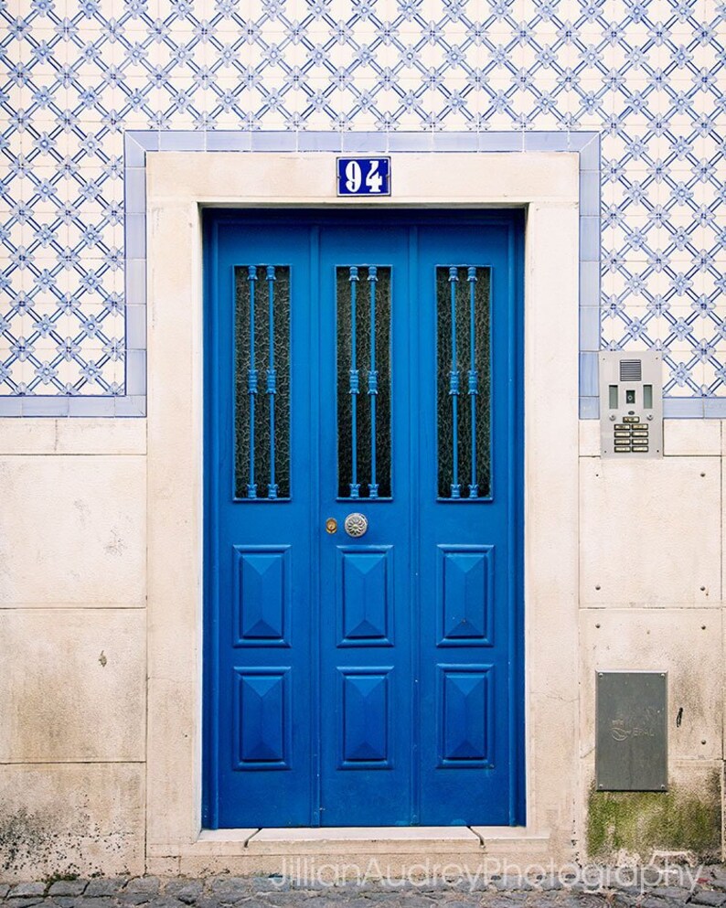 May include: A blue double door with a number "94" above it. The door has a decorative pattern and is set in a white frame. The door is surrounded by white and blue patterned tiles.