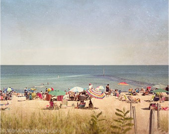 May include: A sunny beach scene with people relaxing under colorful umbrellas. The beach is sandy with a clear blue ocean in the background.