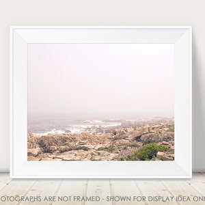 May include: A photograph of a rocky coastline with the ocean in the background. The scene is shrouded in a light mist, giving the image a soft, ethereal feel.