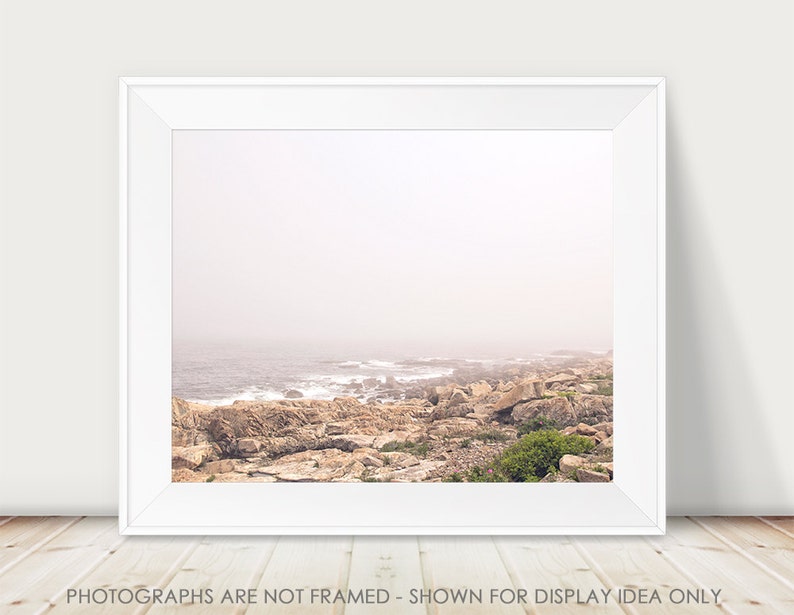 May include: A photograph of a rocky coastline with the ocean in the background. The scene is shrouded in a light mist, giving the image a soft, ethereal feel.