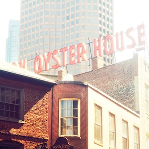 May include: A red neon sign with the words "Union Oyster House" on a brick building. The sign is mounted on a metal frame and is illuminated by bright lights. The building is made of red brick and has a white trim. There is a tall building in the background.