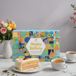 May include: A colorful box of gourmet tea bags with the text "Happy Birthday" and a geometric pattern. The box is next to a slice of cake and two cups of tea on a white table.
