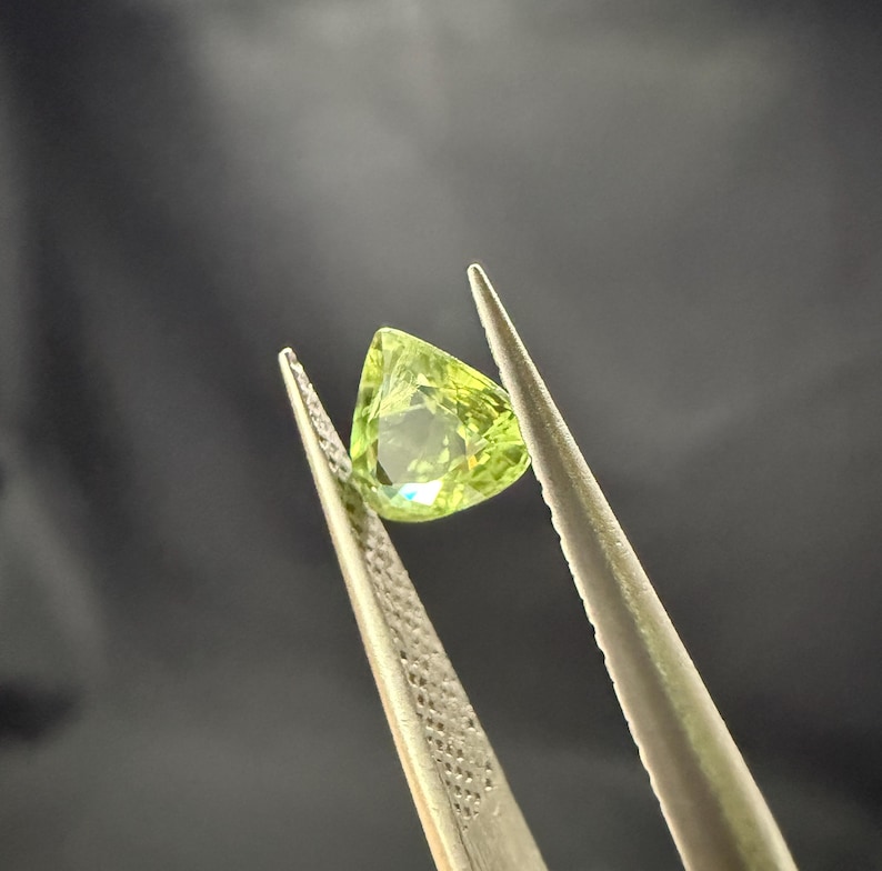 Pode incluir: Uma gema verde com forma triangular, segurada por uma pin&ccedil;a.