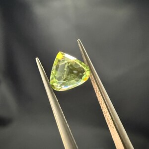 Pode incluir: Uma gema verde com formato triangular, segurada por uma pin&ccedil;a.