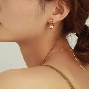 Puede incluir: Pendientes de bola de doble cara de oro. Los pendientes est&aacute;n hechos de un metal liso y brillante y tienen un dise&ntilde;o simple y elegante.