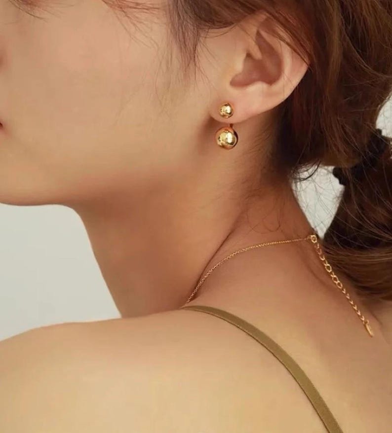 Puede incluir: Pendientes de bola de doble cara de oro. Los pendientes est&aacute;n hechos de un metal liso y brillante y tienen un dise&ntilde;o simple y elegante.