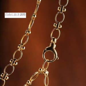 May include: A gold chain necklace with a lobster clasp closure. The chain is made of oval links with small round beads at each link.