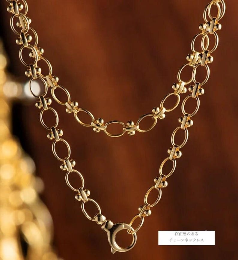 May include: A gold chain necklace with a delicate, oval-shaped link design. The chain features small, round beads along the links, adding a touch of texture. The necklace has a lobster claw clasp.