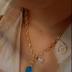 May include: A gold chain necklace with a blue opal pendant and a white pearl charm.