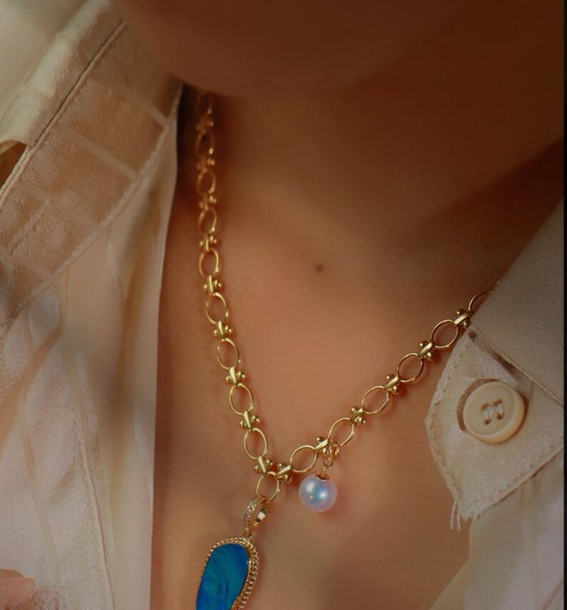 May include: A gold chain necklace with a blue opal pendant and a white pearl charm.