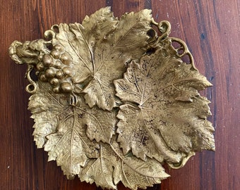 May include: A gold-toned metal grapevine dish with a cluster of grapes in the center. The dish is shaped like a cluster of leaves.