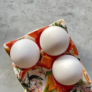 Peut inclure: Un plateau &agrave; &oelig;ufs en c&eacute;ramique orn&eacute; d'un motif color&eacute; d'oranges, de feuilles vertes et de fleurs blanches. Le plateau pr&eacute;sente trois alv&eacute;oles moul&eacute;es, contenant chacune un &oelig;uf blanc, lisse et ovale. Le d&eacute;cor inclut de petites abeilles.