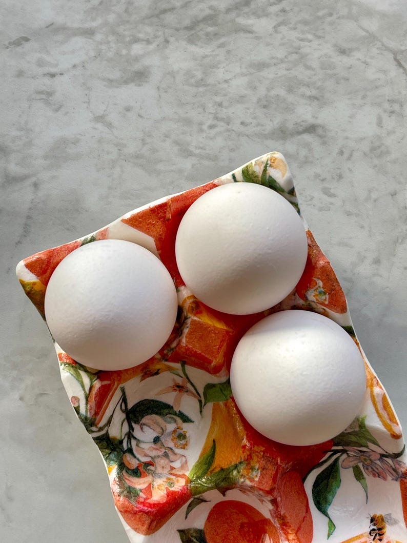 Peut inclure: Un plateau &agrave; &oelig;ufs en c&eacute;ramique orn&eacute; d'un motif color&eacute; d'oranges, de feuilles vertes et de fleurs blanches. Le plateau pr&eacute;sente trois alv&eacute;oles moul&eacute;es, contenant chacune un &oelig;uf blanc, lisse et ovale. Le d&eacute;cor inclut de petites abeilles.