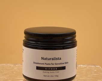 May include: A jar of Naturalista deodorant paste for sensitive skin. The jar is black with a white label that reads "CITRUS" and "Baking Soda Free." The net weight is 2oz/56g. The jar sits on a clear, textured surface against a yellow background.
