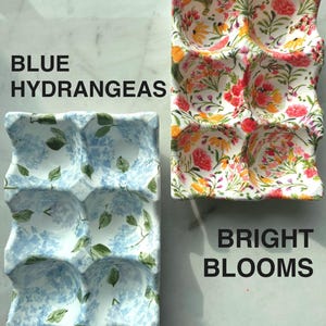 Peut inclure: Deux plateaux &agrave; &oelig;ufs rectangulaires en c&eacute;ramique avec six alv&eacute;oles chacun. Le plateau de gauche pr&eacute;sente un motif d'hortensias bleus avec des feuilles vertes, marqu&eacute; BLUE HYDRANGEAS. Le plateau de droite affiche un motif floral color&eacute;, marqu&eacute; BRIGHT BLOOMS.